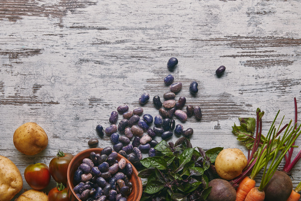 violette Haricot-Bohnen und rohes Gemüse zum Kochen auf rustikalem Holztisch - Foto, Bild