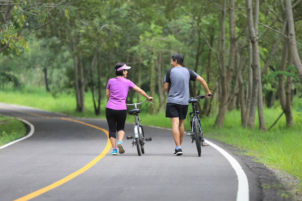 Pareja de mediana edad ejercicio relajante con bicicleta en el parque
 - Foto, Imagen