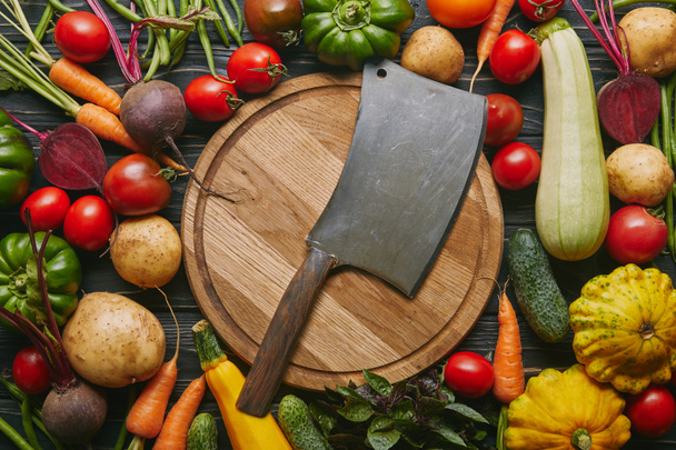 Metal cleaver on cutting board with colorful vegetables on dark wooden table - Photo, Image