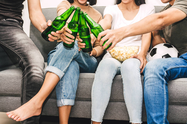 Группа друзей, которые едят попкорн и пьют пиво вместе и смотрят футбол на диване в домашних условиях.
 - Фото, изображение