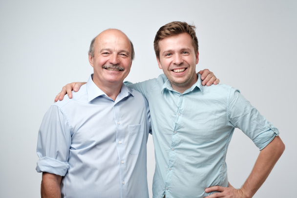 Hispanic father and adult son hugging and smiling at camera. Good famile relations. - Photo, image