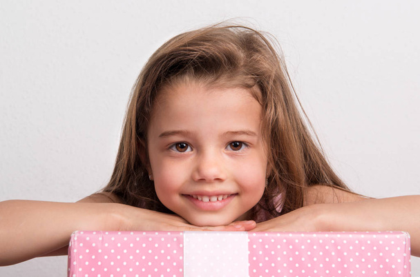 Portrait of a small girl in studio, her head resting on a wrapped box. - Foto, imagen