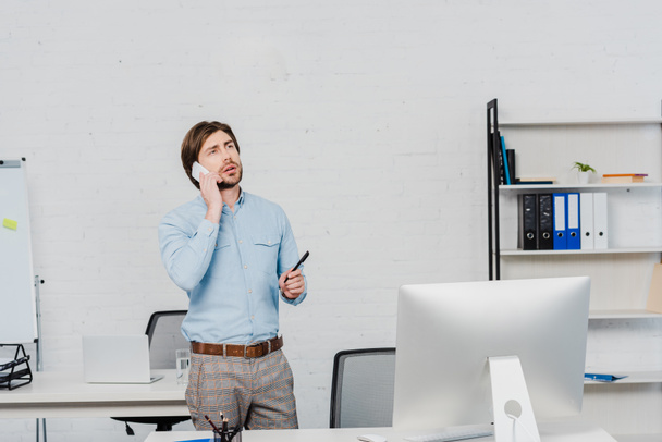 emotional young businessman looking up while talking by phone at modern office - Foto, Bild