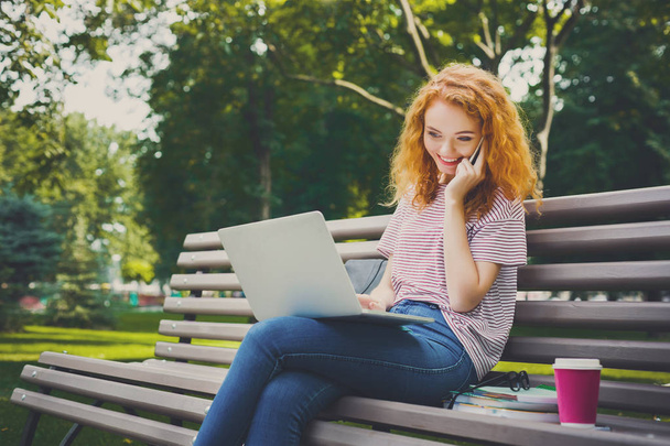 Kızıl saçlı öğrenci kız cep telefonu ve dizüstü bilgisayar üzerinde konuşuyor - Fotoğraf, Görsel