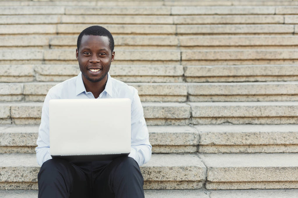 屋外でノート パソコンでの作業幸せのアフリカ系アメリカ人のビジネスマン - 写真・画像