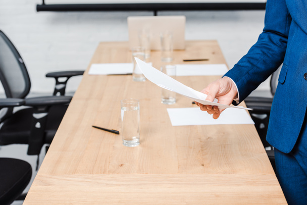 обрезанный снимок бизнесмена, держащего пустую бумагу за столом для конференций в офисе
 - Фото, изображение