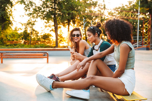Три возбужденные молодые девушки веселятся, сидя со скейтбордом в парке
 - Фото, изображение