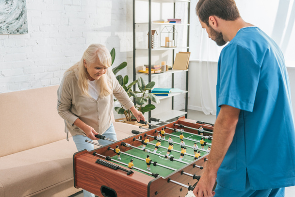 high angle view of senior woman playing table football with social worker - Foto, Imagem