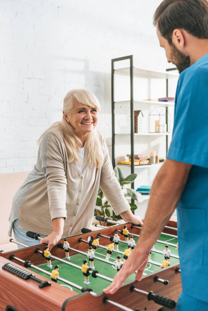 smiling senior woman playing table football with social worker - Фото, изображение