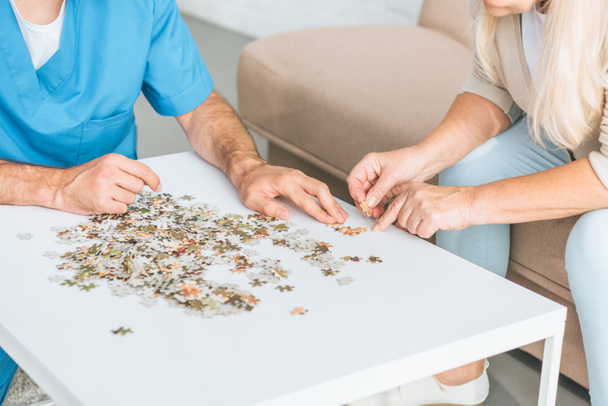 cropped shot of senior woman and young social worker playing with puzzle pieces - Fotoğraf, Görsel