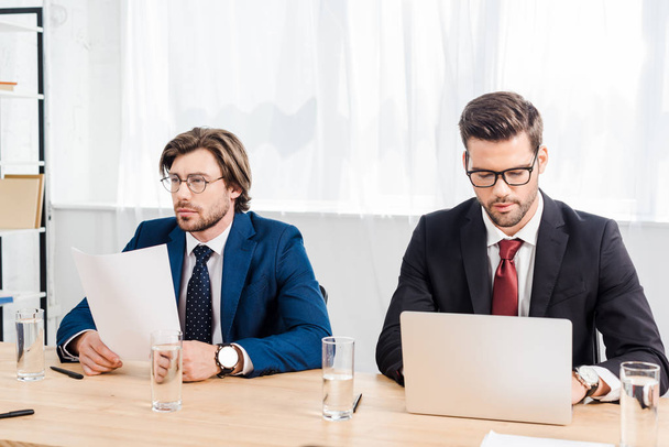 hommes d'affaires prospères travaillant avec des documents et un ordinateur portable ensemble au bureau moderne
 - Photo, image