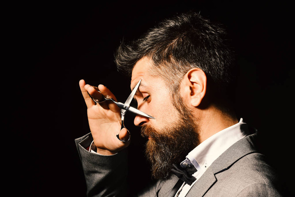 Man with long beard holds steel scissors near eyes. Business and barbershop service concept. Businessman with tricky face - 写真・画像