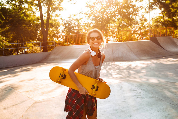 Photo of young happy cheerful woman walking outdoors with skateboard. - Фото, зображення