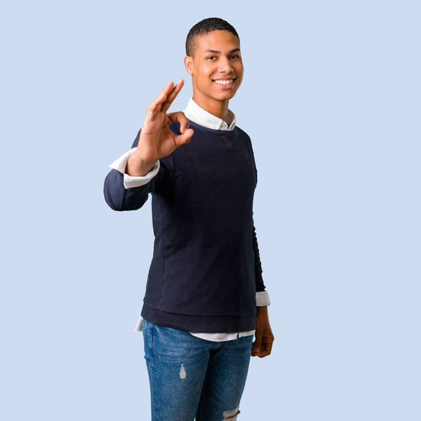 Nuori afrikkalainen amerikkalainen mies osoittaa ok merkki sormet eristetty sininen tausta
 - Valokuva, kuva