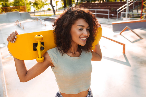 Photo of young happy cheerful woman walking outdoors with skateboard. - Zdjęcie, obraz