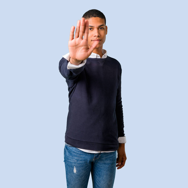 Jeune homme afro-américain faisant un geste d'arrêt avec sa main sur fond bleu isolé
 - Photo, image