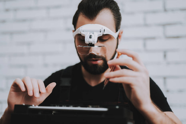 Young Man Repairing Hardware Equipment in Repair Shop. Worker with Tools. Computer Hardware. Electronic Devices Concept. Bearded Man. Modern Devices. Digital Device. Man in Glasses. - 写真・画像