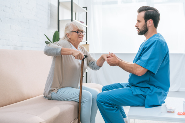 side view of male nurse helping senior woman with walking stick - Photo, Image