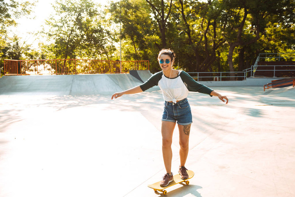 Photo of young happy cheerful woman walking outdoors with skateboard listening music. - Zdjęcie, obraz
