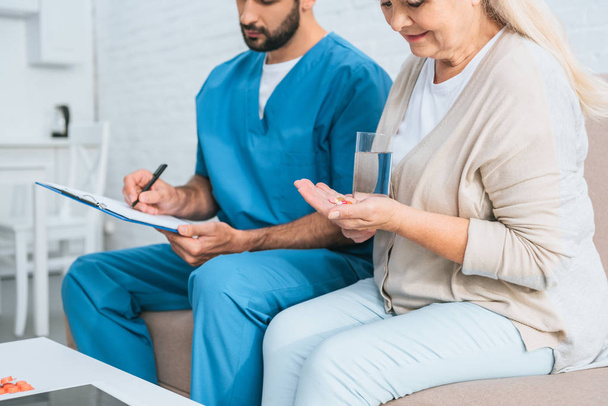 cropped shot of senior woman taking medicine and male nurse writing on clipboard - Foto, Imagen