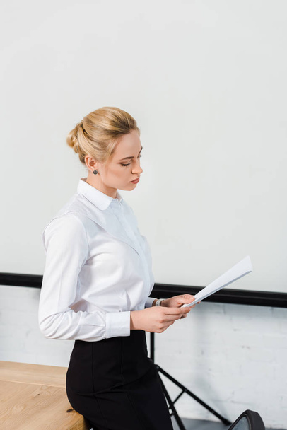 focused young businesswoman reading documents in front of blank presentation board - Foto, Imagem
