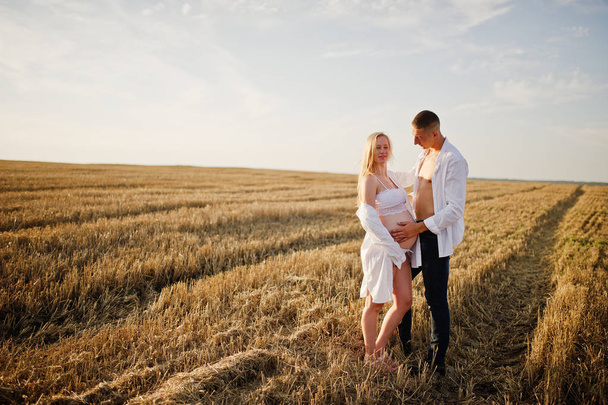 Беременная пара в поле для венков на белом нижнем белье на закате. Счастливые моменты беременности
. - Фото, изображение
