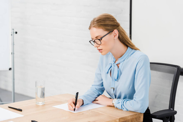 beautiful young businesswoman writing on blank paper at modern office - Foto, Imagem