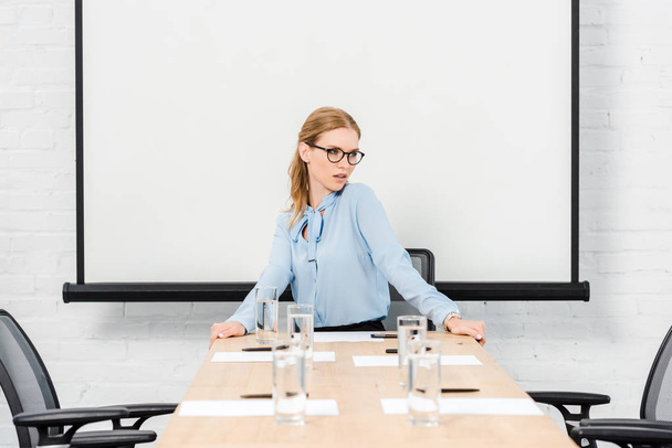 attractive young businesswoman sitting alone at conference hall and looking away - 写真・画像