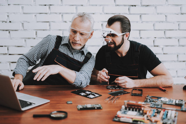 Two Men Repairing Mobile Phone in Modern Workshop. Repair Shop. Young and Old Workers. Digital Device. Man in Glasses. Electronic Devices Concept. Mobile Device Hardware. Workers with Tools. - Foto, Imagen