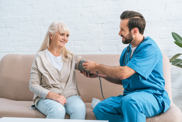 sorridente infermiera di sesso maschile che misura la pressione sanguigna alla donna anziana
 - Foto, immagini