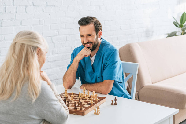 senior woman playing chess with smiling young social worker - Foto, Bild