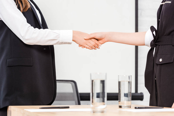обрезанный снимок бизнесвумен, пожимающих руку в современном офисе
 - Фото, изображение