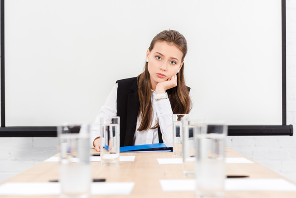 bored young businesswoman sitting at table in conference hall at modern office and looking at camera - Foto, Imagem