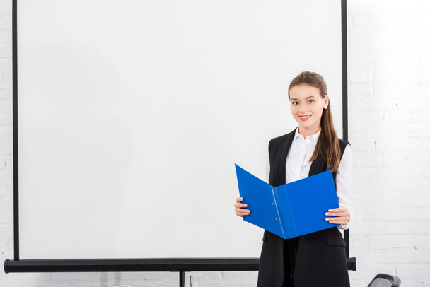 attractive young businesswoman with folder in front of blank whiteboard at modern office - Fotografie, Obrázek