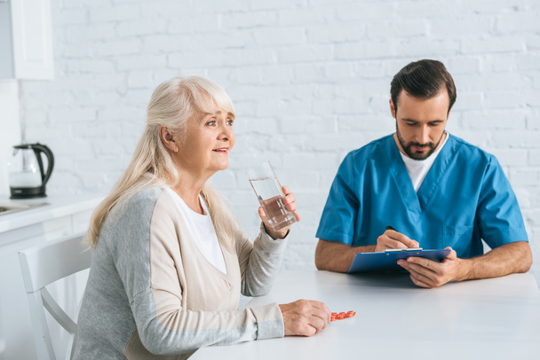 соціальний працівник пише в буфері, коли усміхається старша жінка приймає таблетки
 - Фото, зображення
