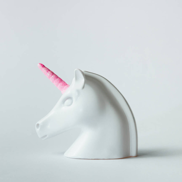 Wit geschilderd unicorn hoofd met roze hoorn op helder witte achtergrond. Minimal art fantasie concept. - Foto, afbeelding