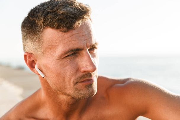 Gros plan du beau sportif torse nu avec écouteurs à la plage
 - Photo, image
