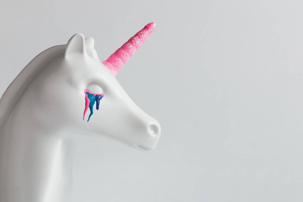 Cabeza unicornio pintada de blanco con lágrimas de colores y cuerno rosa sobre fondo blanco brillante. Concepto de fantasía de arte mínimo
. - Foto, Imagen