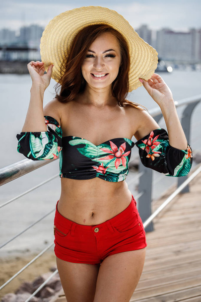 Outdoor portrait of beauty brunette model in colorful summer clothes. Young beautiful woman standing on embankment at daytime, blurred background  - Valokuva, kuva