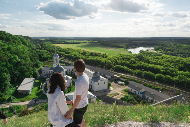 young couple travels standing on a hill and admiring the magnificent views of the valley, river and monastery - Photo, Image