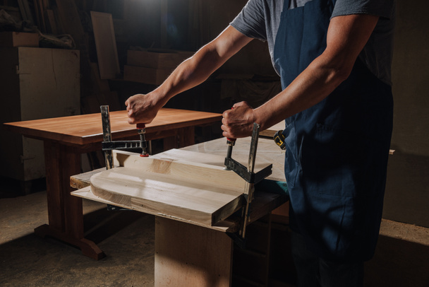 tiro cortado de carpintero en delantal trabajando en madera en el taller
 - Foto, Imagen