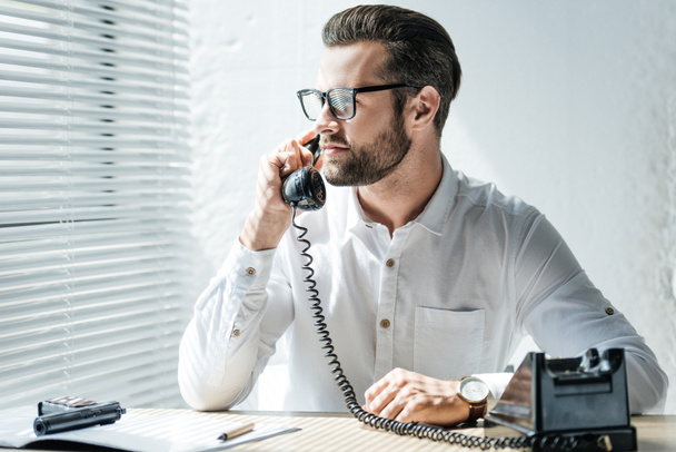 bearded businessman talking on rotary telephone at workplace with weapon - Foto, Imagem
