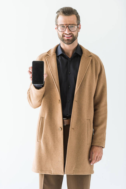 bärtiger lächelnder Mann präsentiert Smartphone mit leerem Bildschirm, isoliert auf weiß - Foto, Bild