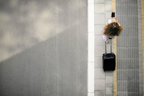 Pohled shora ženy držící chytrý telefon a zavazadel při cestě na nádraží/letiště. - Fotografie, Obrázek