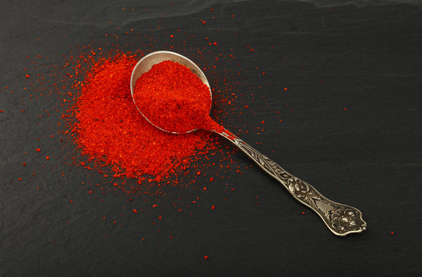 Fermer une cuillère vintage en métal antique pleine de piment rouge ou de poudre de paprika sur fond de panneau d'ardoise noire, vue grand angle
 - Photo, image