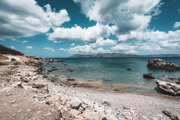 Panoramic view of rocks and beach with sky and clouds in Crete, Greece. Amazing scenery with crystal clear water and the rock formation against a deep blue sky during Summer period. Greece, Europe - Фото, изображение