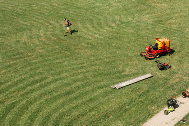 男は、広い分野での芝刈機で動作します。トップ ビューの背景。Web サイト、パンフレット、広告のテキストのためのスペース。天気は、明るく温かみのある色調。草線のパターン。外の完成した作品 - 写真・画像