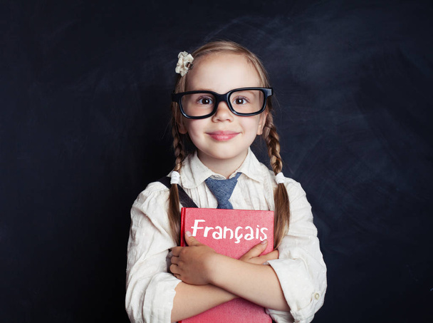 Poika opiskelee ranskaa kielikoulussa. Onnellinen pieni tyttö pitää kirjaa käsissään liitutaulussa
 - Valokuva, kuva