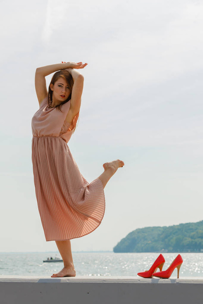 Hobby, idyllic aspects of femininity concept. Woman dancing on jetty without shoes wearing beautiful long light pink dress. - Foto, afbeelding