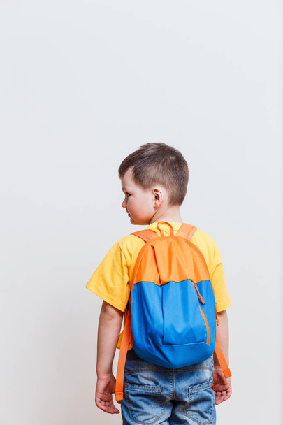 little boy with a backpack stands back on a white background - Foto, afbeelding